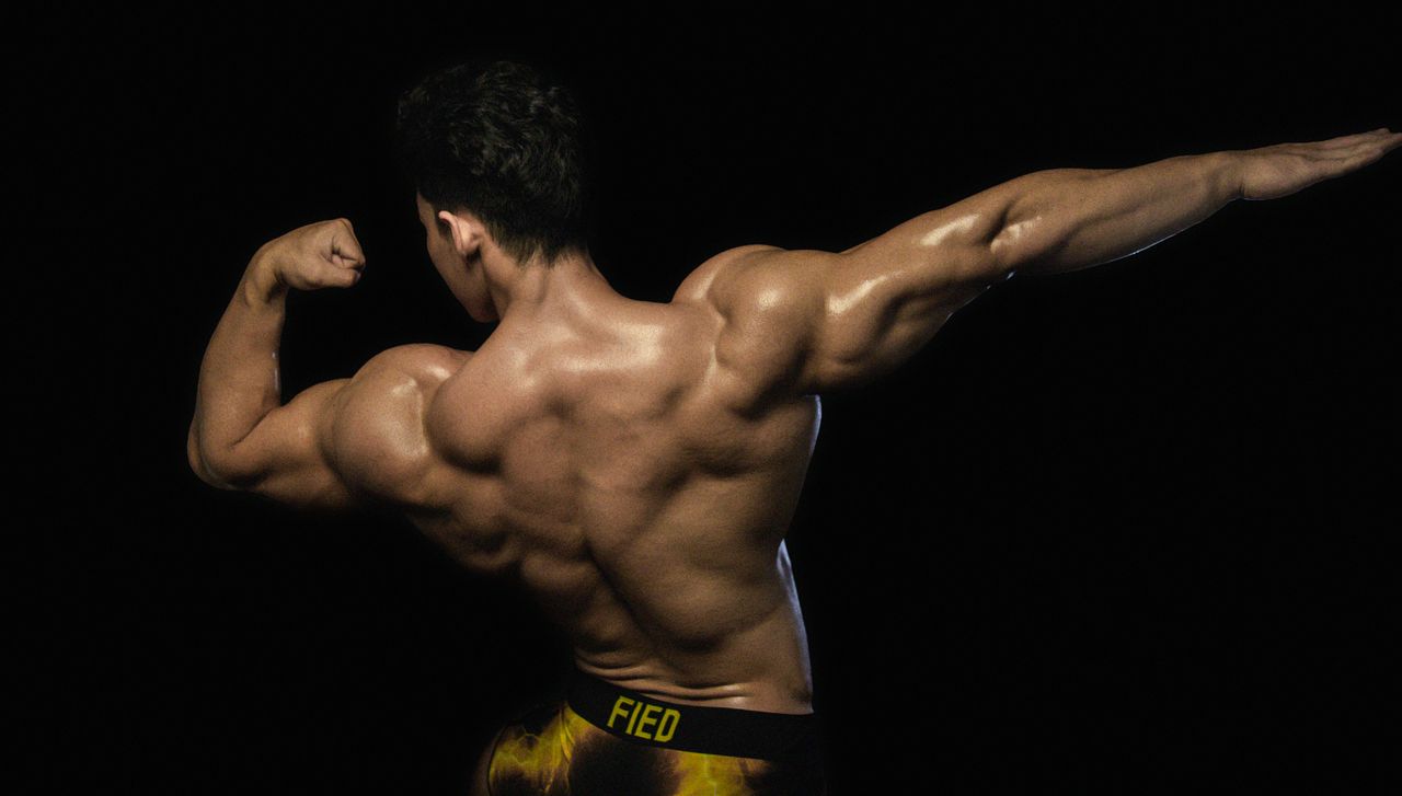 back view of a male bodybuilder flexing muscles against a dark backgro