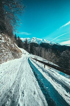 A scenic snowy roadway in winter, leading to snow-capped mountains in Lombardy, Italy.