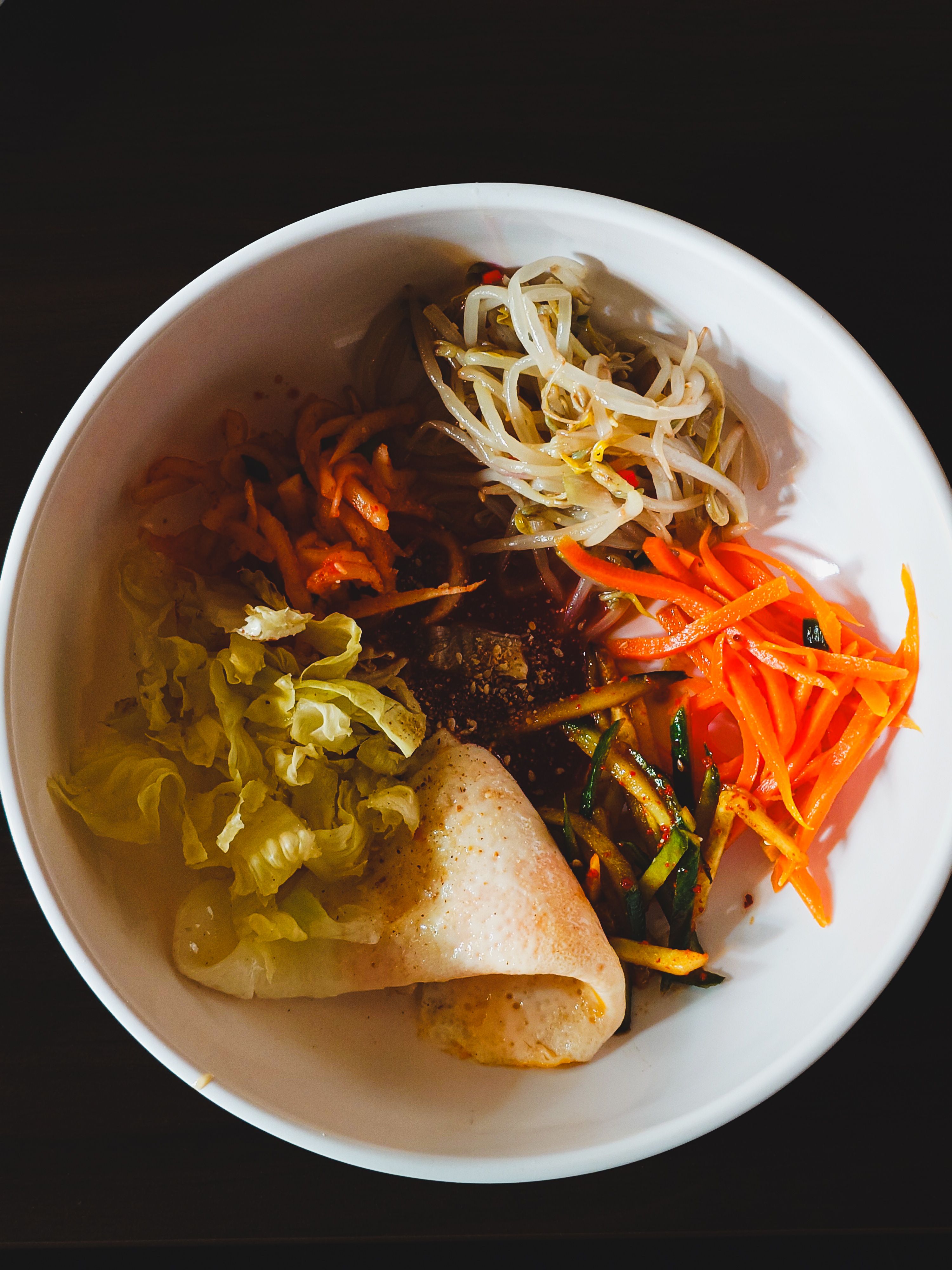 Top view of a vibrant Korean bibimbap dish with assorted vegetables in a white bowl.