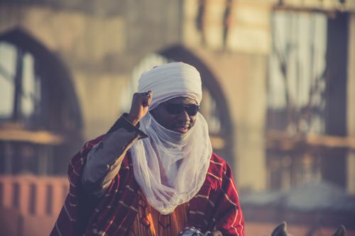 Free Portrait of a man in traditional African attire wearing sunglasses, with a blurred architectural backdrop. Stock Photo