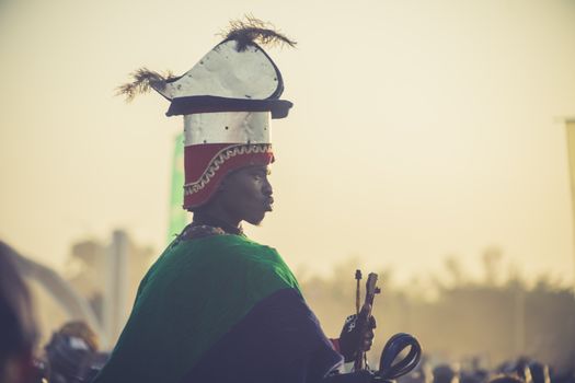 A person in traditional festival attire with a large, ornate headpiece at an outdoor event.
