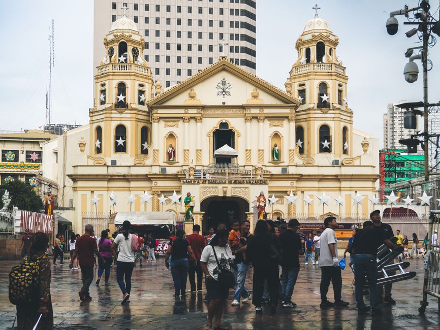 People gather in front of the historic Quiapo Church in Manila, Philippines. A vibrant urban scene.