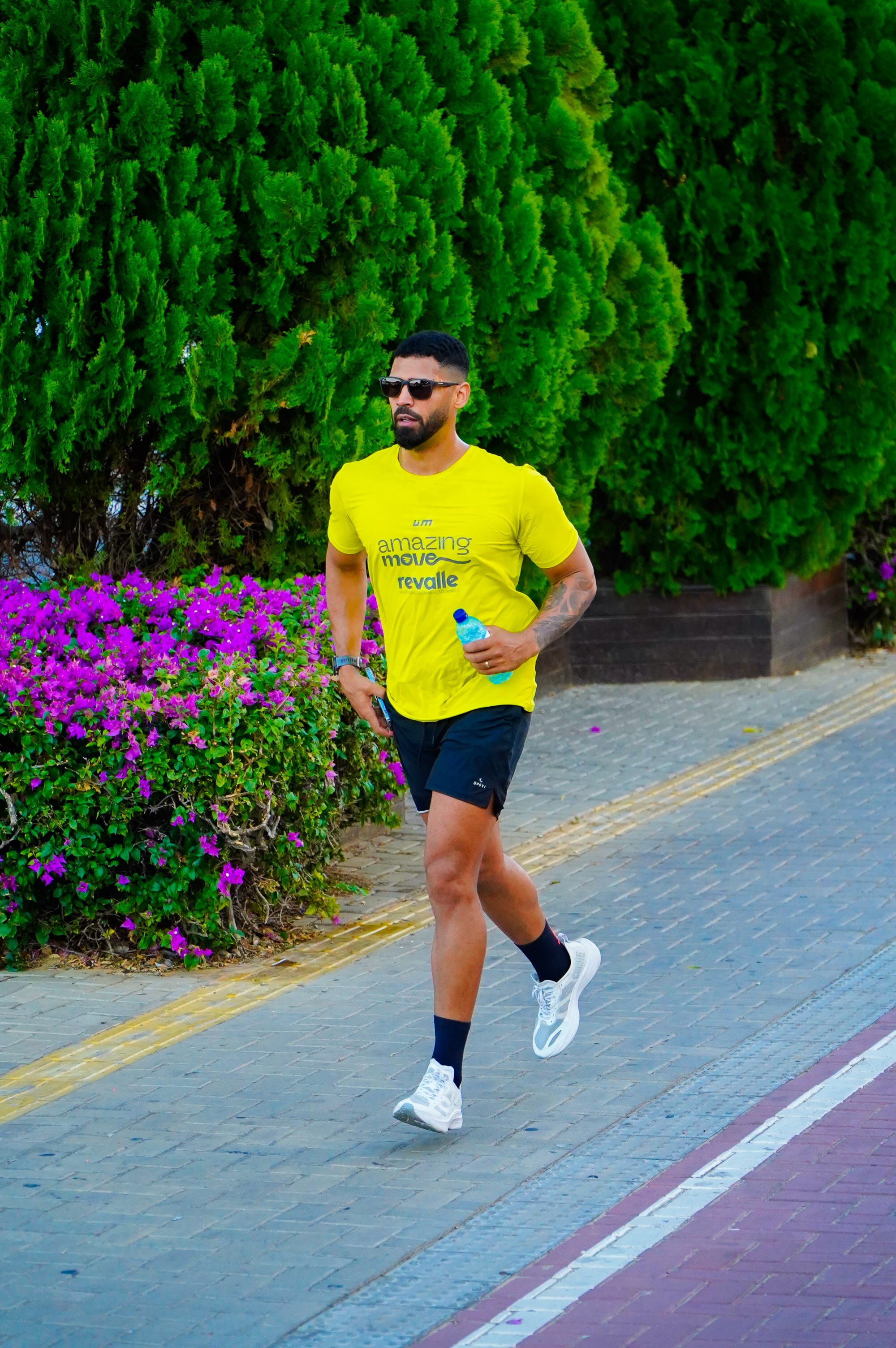 Fotomural Un hombre adulto corre por un sendero a plena luz del día, con gafas de sol y una camiseta amarilla.