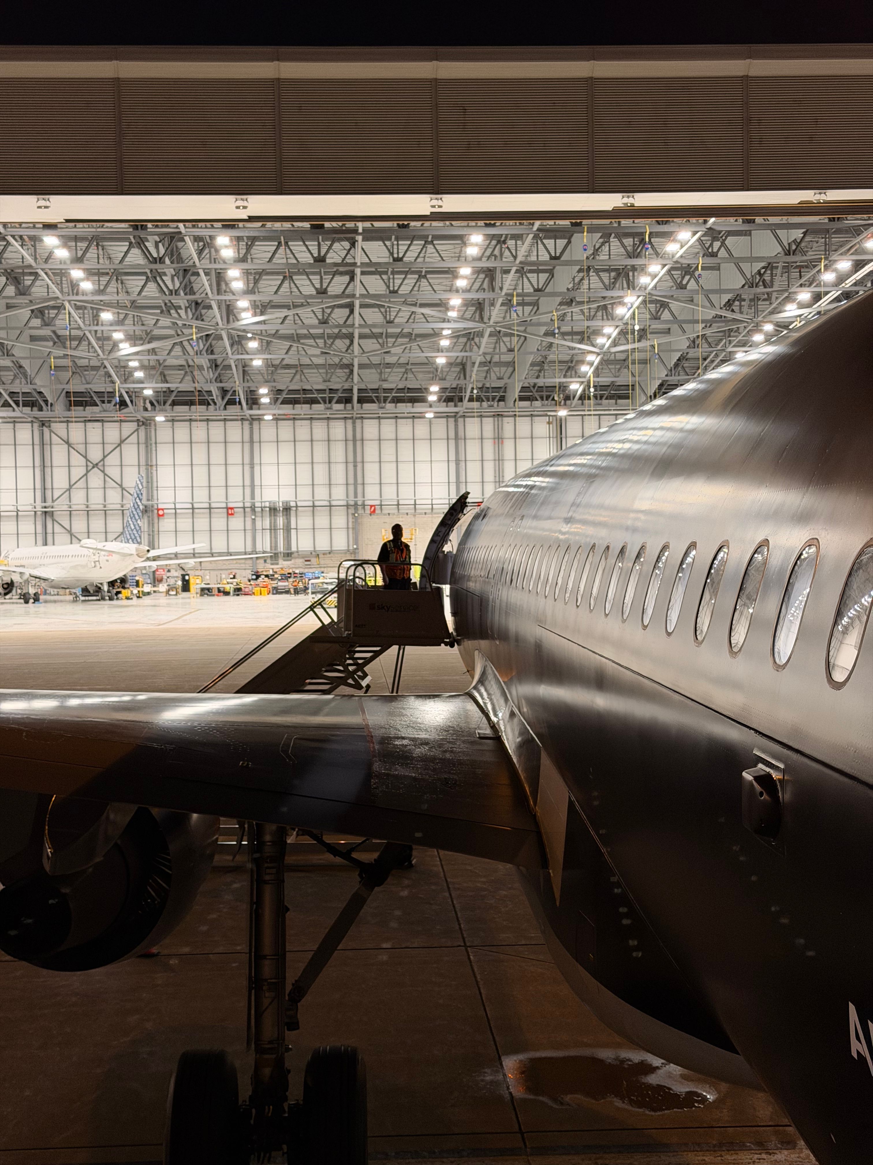 Nighttime photo of airplane maintenance in a hangar with visible aircraft and crew.