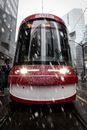 在白雪皑皑的多伦多市中心街道上，一辆红色电车正在行驶
