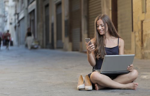 Photo De Femme Assise Sur Le Sol Tout En Utilisant Un Smartphone Et Un Ordinateur Portable