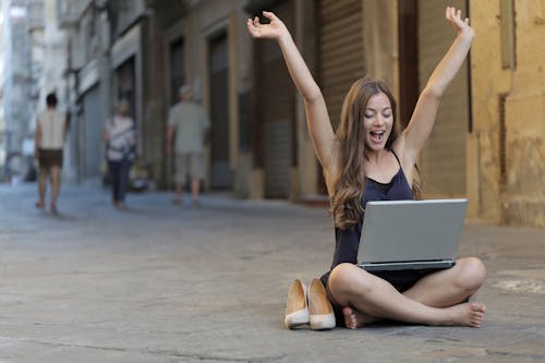 Free Woman Raising Her Hands Up While Sitting on Floor With Macbook Pro on Lap Stock Photo