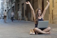 Woman Raising Her Hands Up While Sitting on Floor With Macbook Pro on Lap