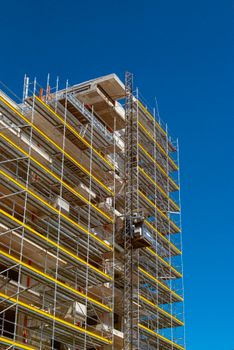 A modern high-rise building under construction with scaffolding against a clear blue sky.