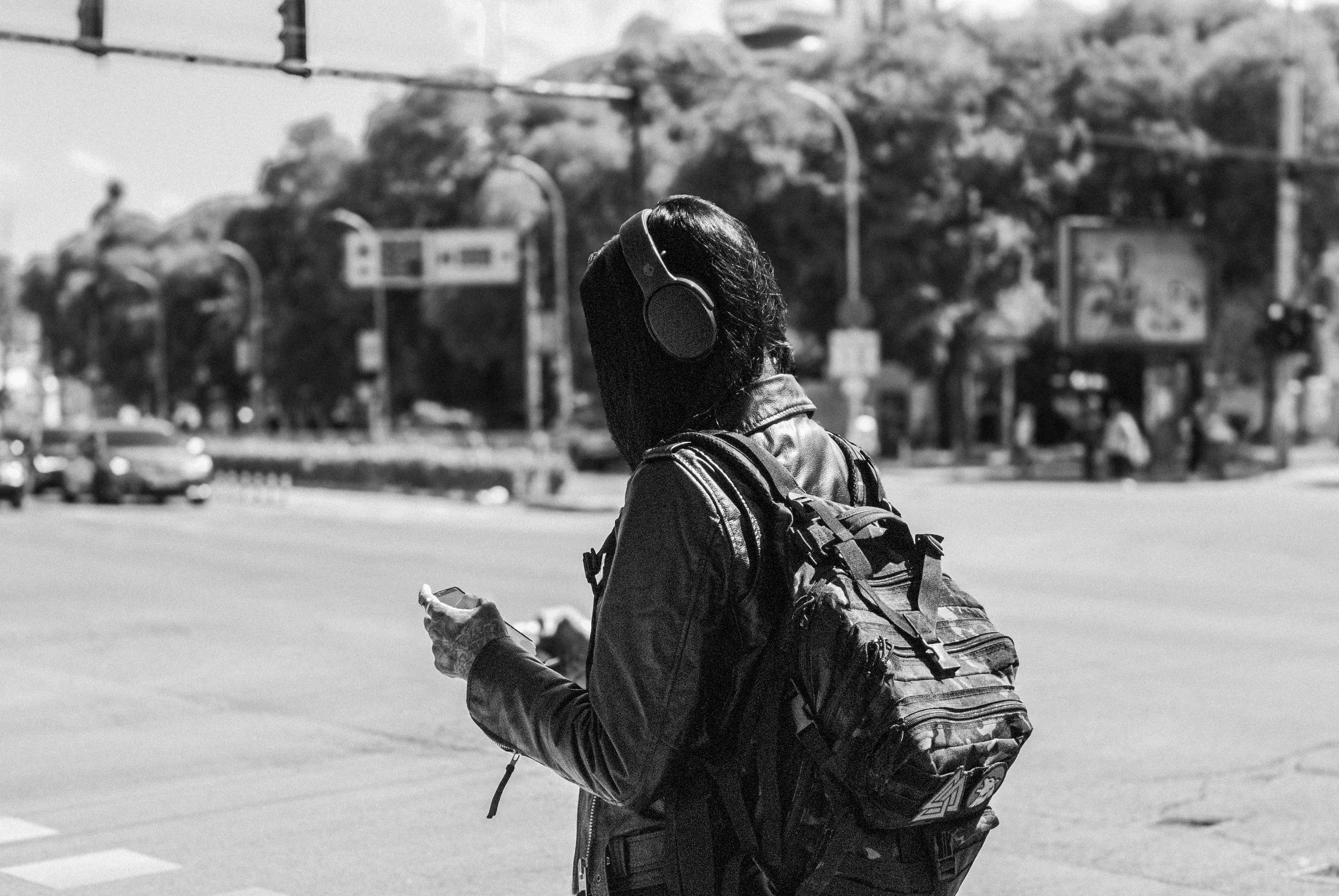 Back view of a person with headphones crossing a street in a city setting.