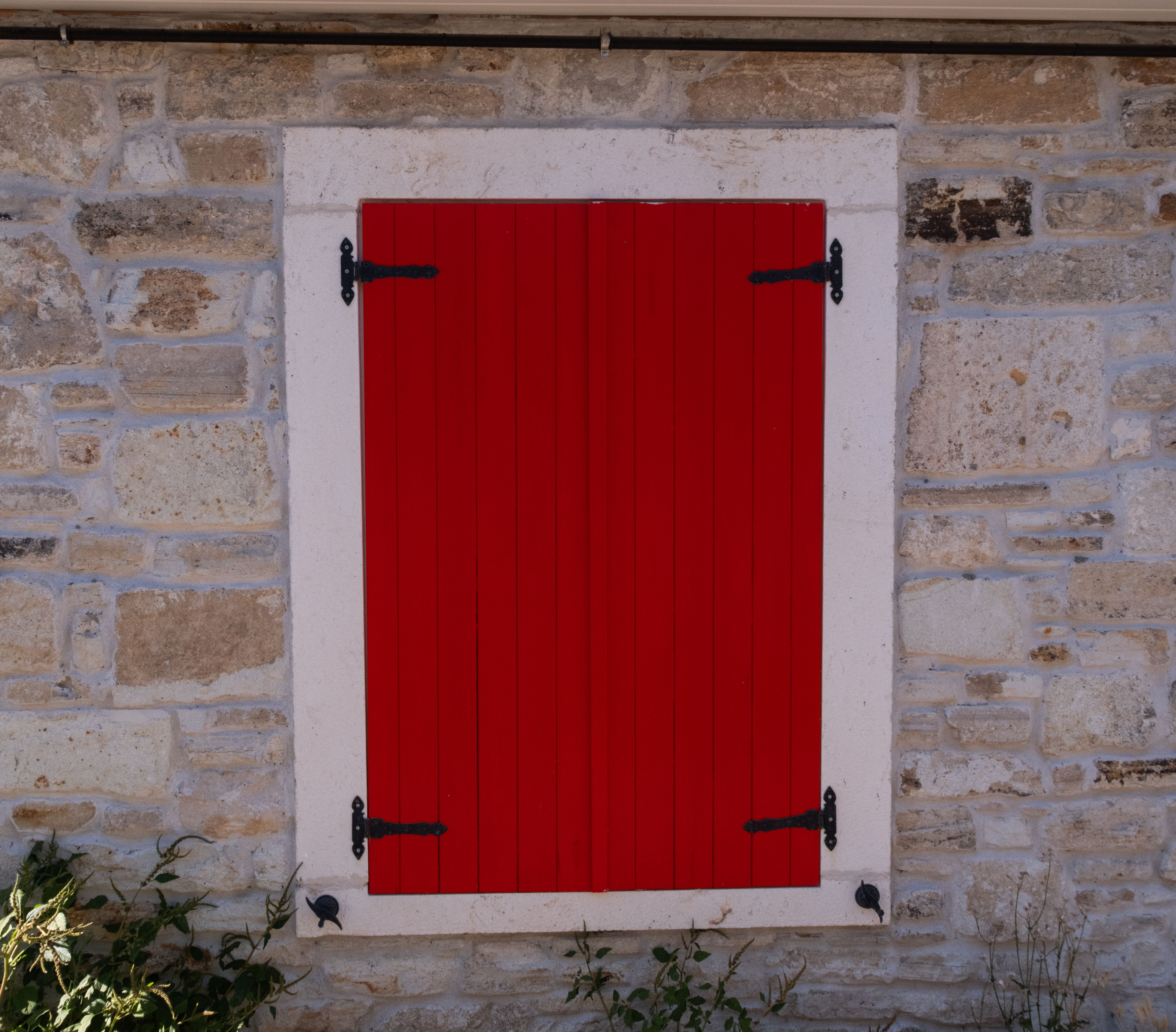 Vivid red shutter on a rustic stone wall in Foça, İzmir, Türkiye, highlighting architectural charm.