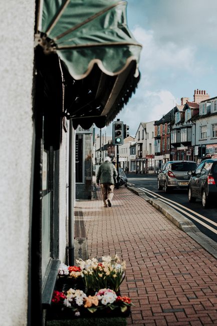 A quaint urban street in Abergele, Wales with pedestrians and vibrant flowers.