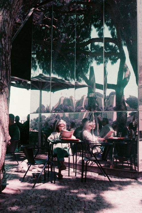 Free Vintage reflection of people at a Lisbon café, surrounded by trees and mirrors. Captivating and serene. Stock Photo