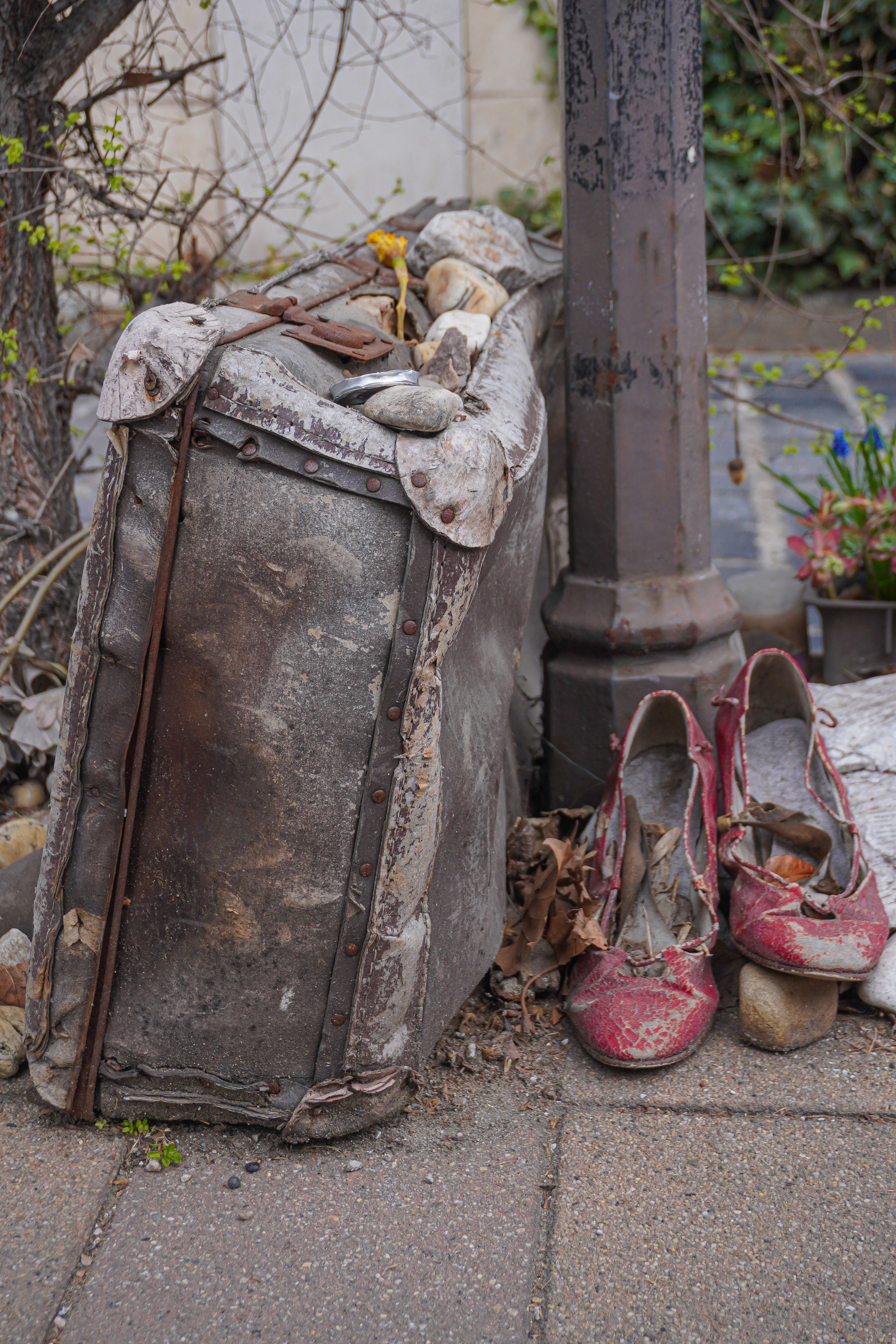 Weathered suitcase and red shoes on a sidewalk signal past journeys and stories left behind.