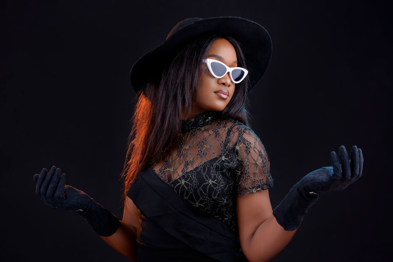 elegant woman in black attire hat gloves and sunglasses posing against