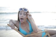 一位穿着比基尼的女人靠在沙滩椅上，表情俏皮