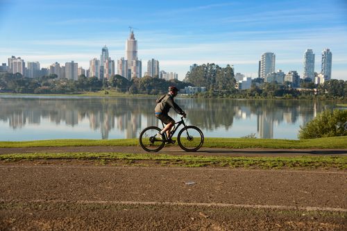 Free A person cycling along a pathway with a vibrant city skyline and lake in Paraná, Brazil. Stock Photo