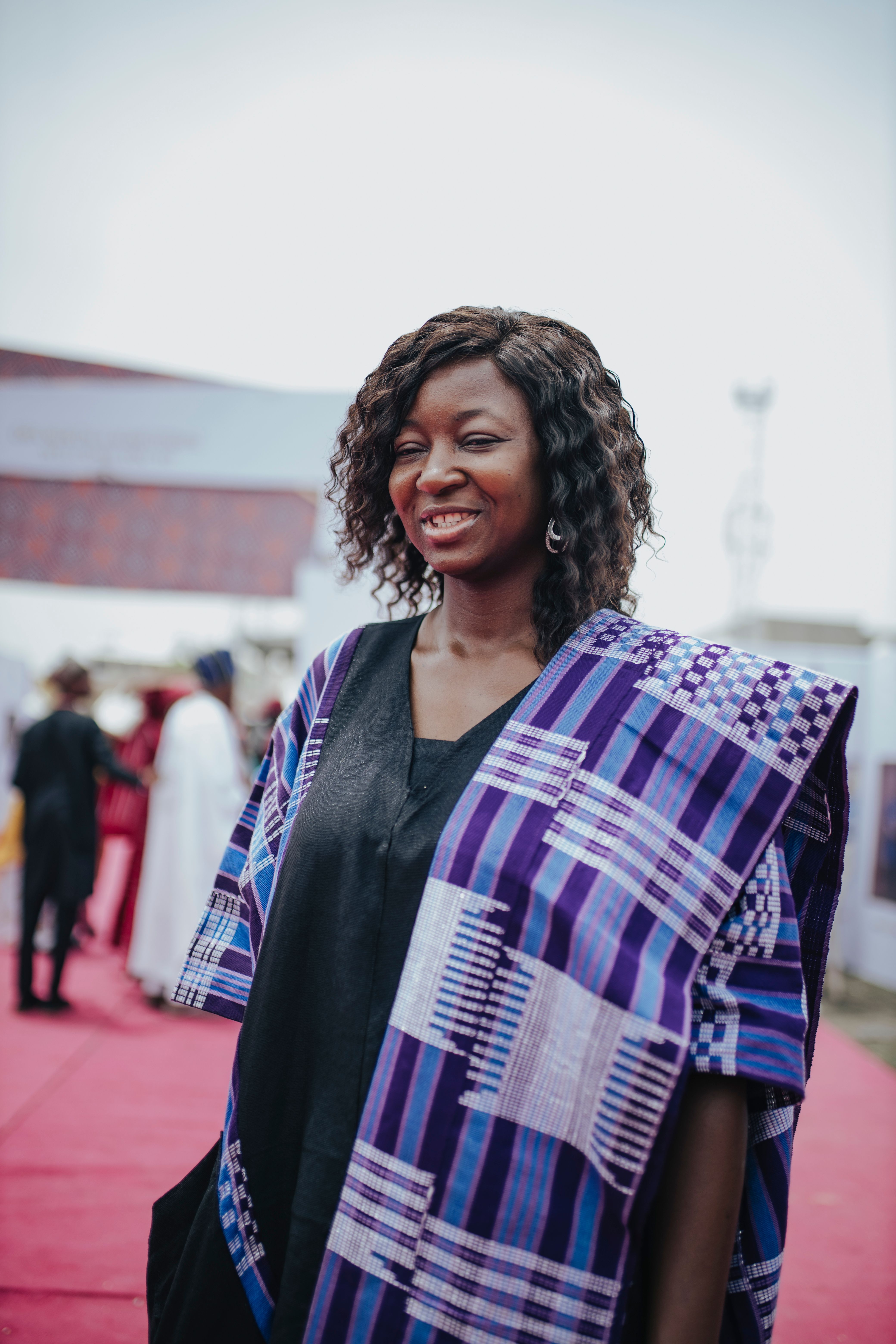 Woman in traditional African clothing smiling at outdoor event.