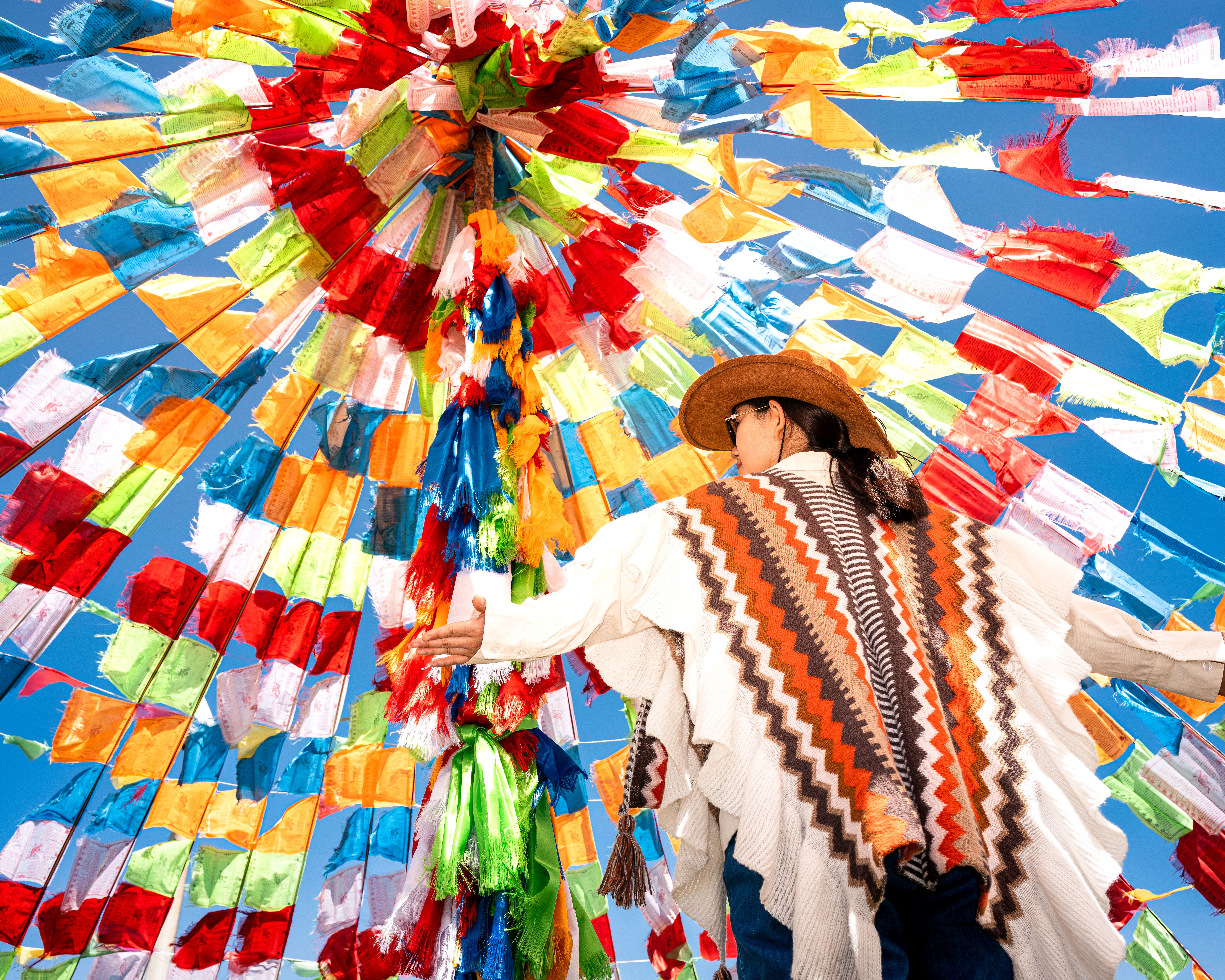 Person in traditional attire under a canopy of vibrant flags in Ulanqab, China.