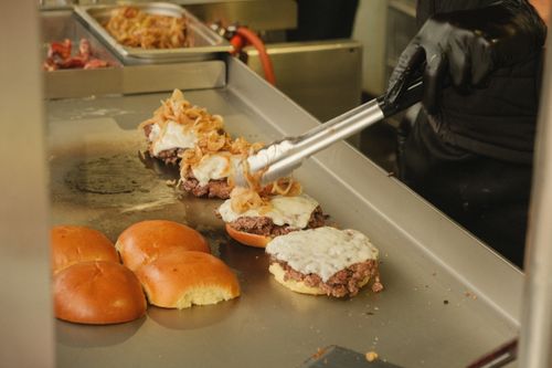 Free Close-up of cheeseburgers with caramelized onions being prepared on a grill, capturing the essence of a classic American meal. Stock Photo