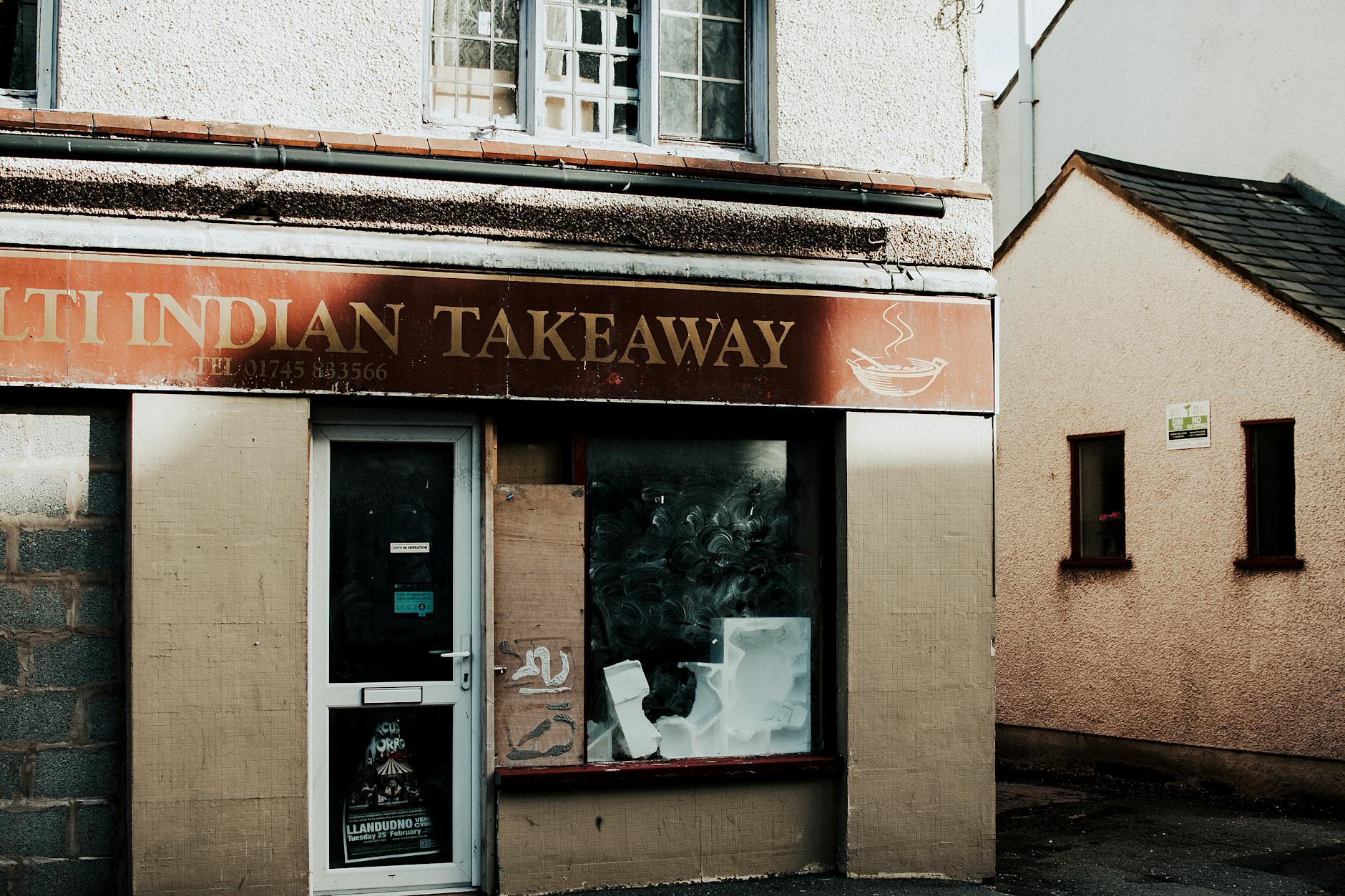 Exterior shot of an abandoned Indian takeaway restaurant with visible signage and boarded windows.