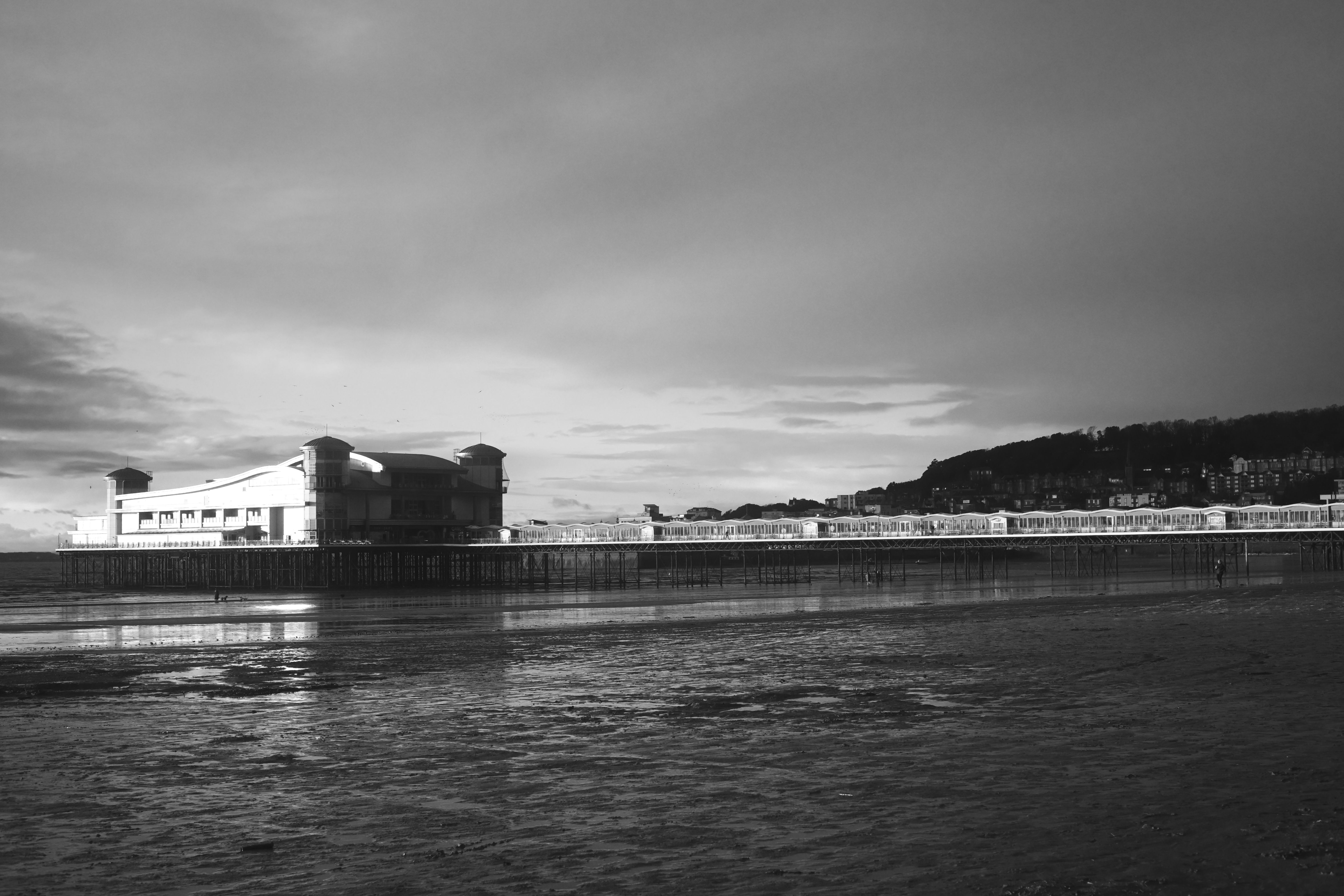 Dramatic black and white photo of a seaside pier under a cloudy winter sky.