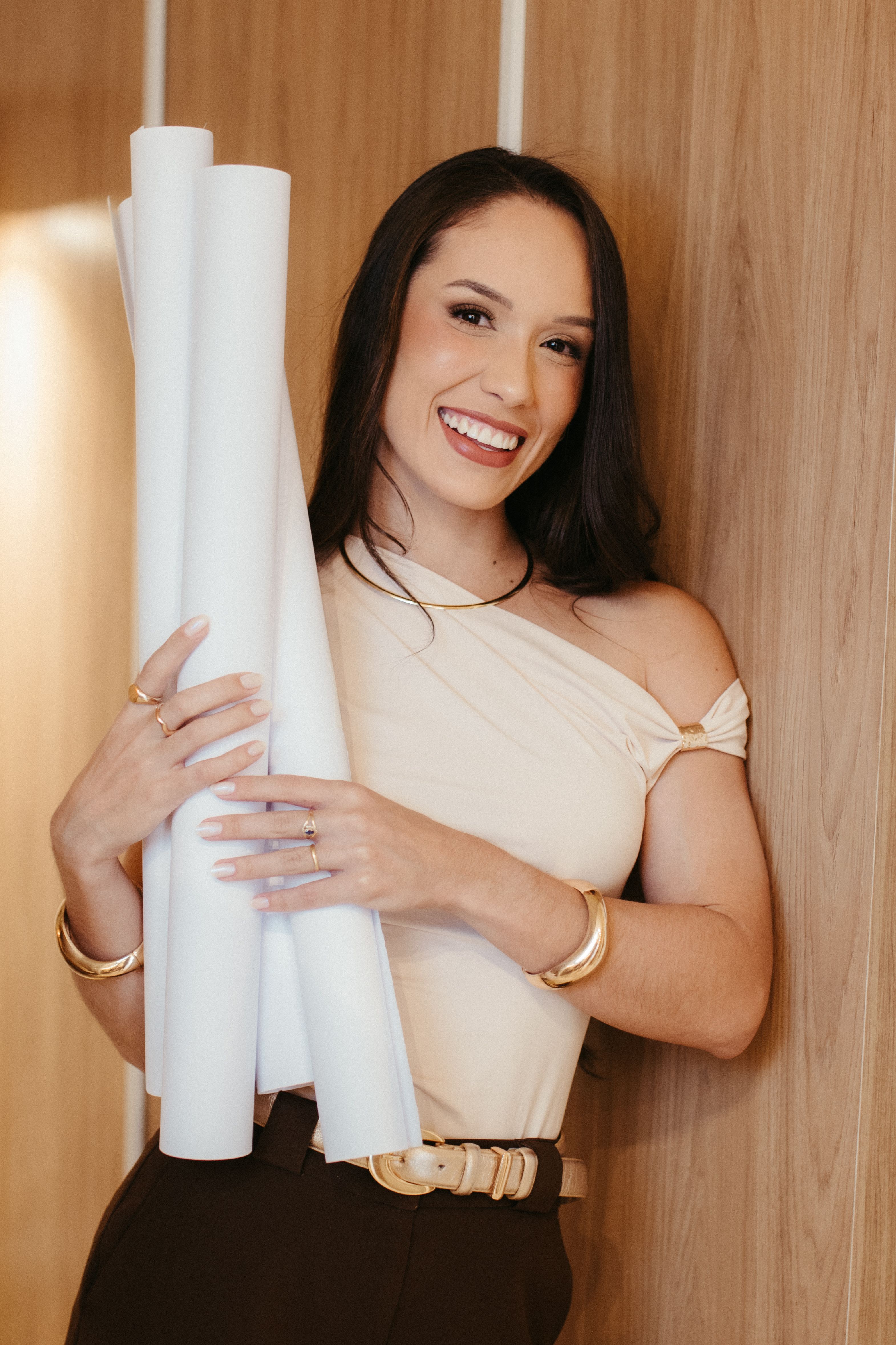 Smiling young woman in elegant dress holding blueprints. Indoor setting.