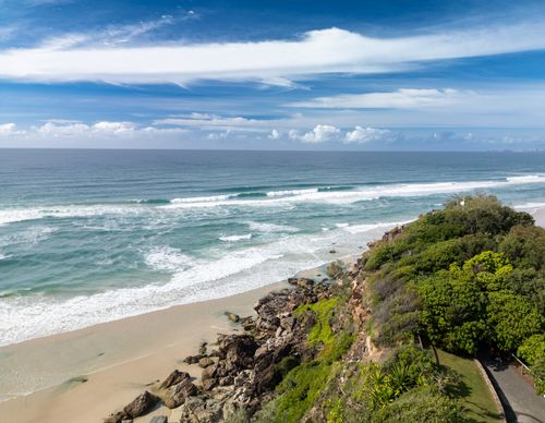 Free A stunning view of the coastline featuring lush greenery, rocky cliffs, and tranquil ocean waves under a clear sky. Stock Photo