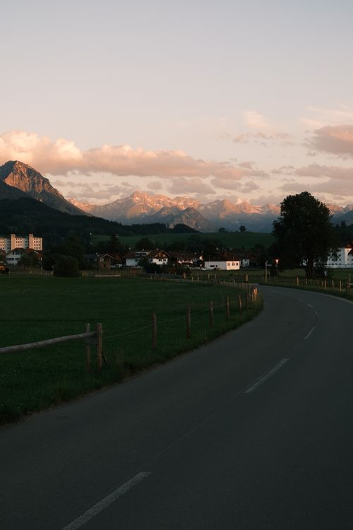 Free Idyllic village with mountain backdrop and winding road at sunset. Stock Photo