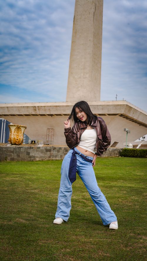 Free Smiling woman posing in front of Jakarta's iconic National Monument under a blue sky. Stock Photo