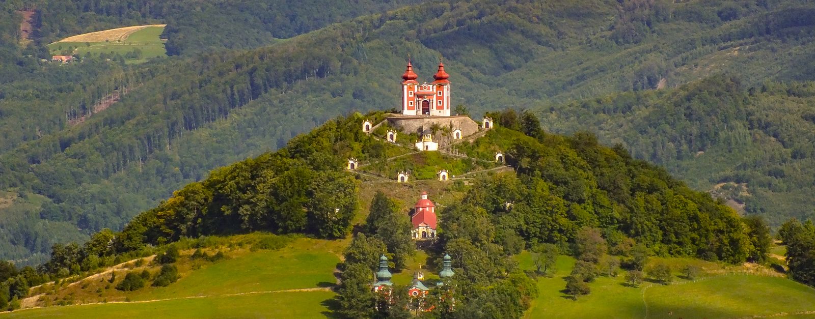 A stunning landscape of the Calvary of Banská Štiavnica on a lush hillside surrounded by green forests.