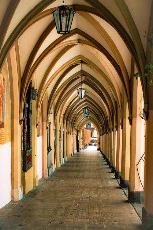 Free A long corridor with Gothic arches and hanging lanterns, offering a medieval architectural charm. Stock Photo