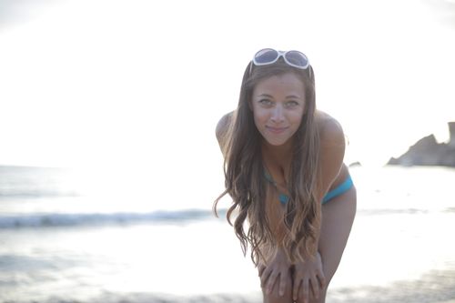 Free A woman with sunglasses smiles on a bright summer beach, enjoying the sun. Stock Photo