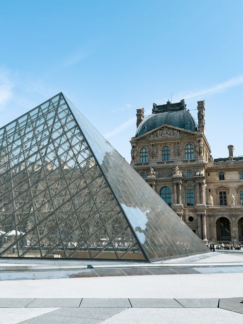 Free The iconic glass pyramid at the Louvre Museum in Paris surrounded by historical architecture. Stock Photo
