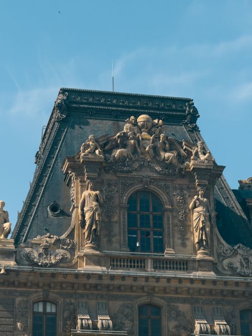 Free Close-up of a decorative facade with sculptures at the Louvre Museum in Paris, under clear blue sky. Stock Photo