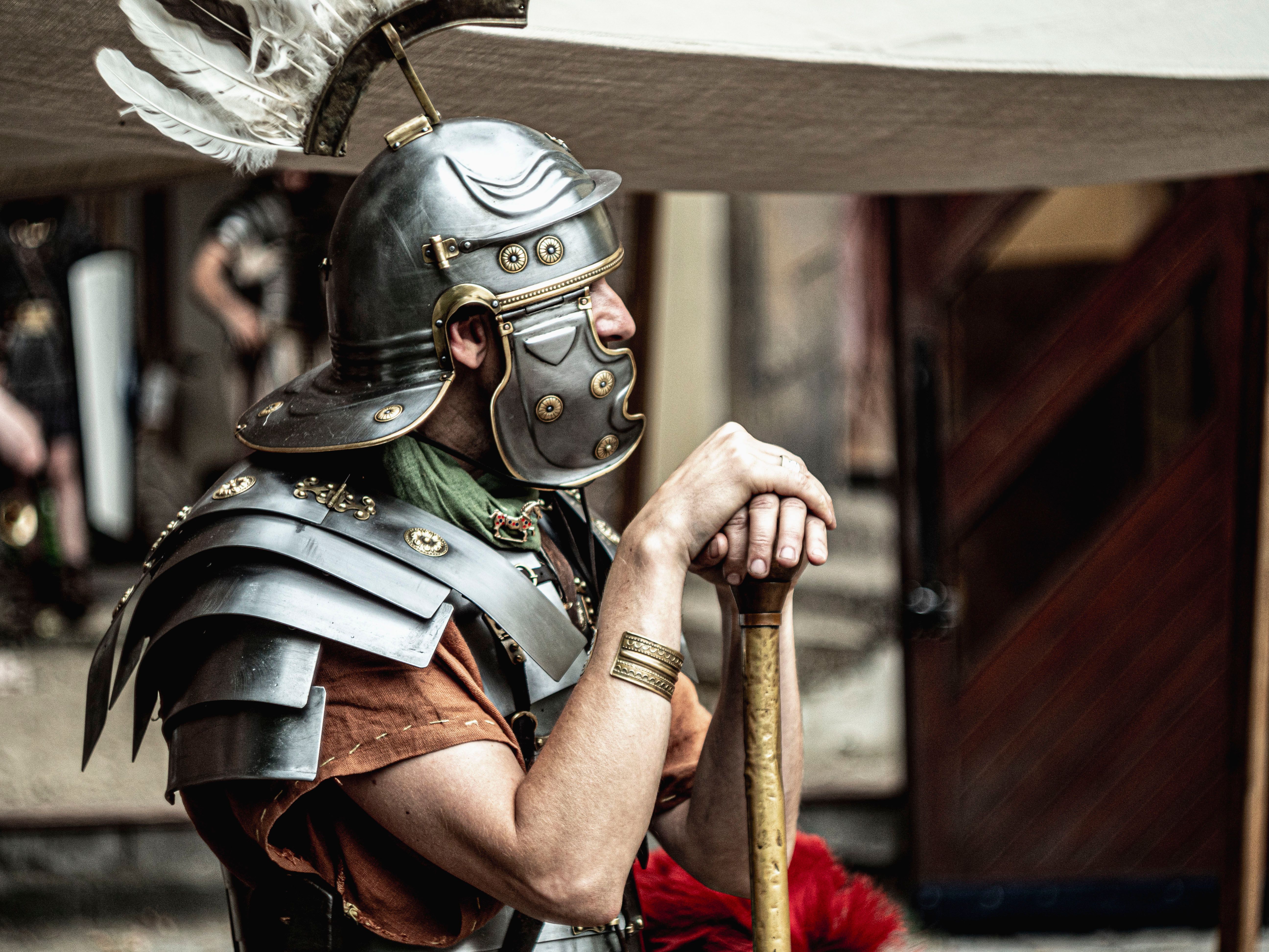 Side profile of a Roman soldier reenactor in detailed armor, thoughtful pose.
