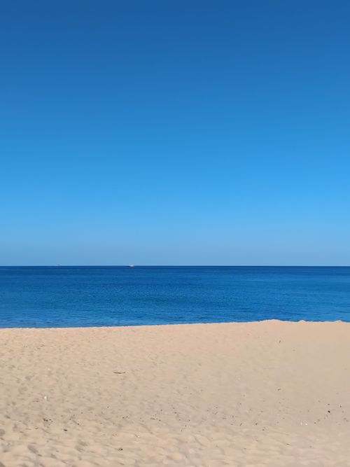 Free A serene sandy beach under a clear blue sky, perfect for relaxation and summer vacations. Stock Photo