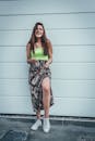 一位自信的年轻女子身着花卉裙子和霓虹灯上衣，在户外靠着白墙微笑