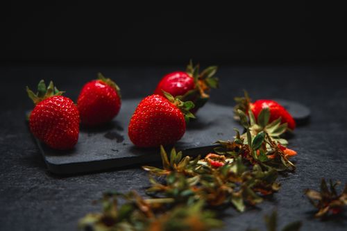 Free Vibrant fresh strawberries on a dark slate with scattered leaves, creating a colorful contrast. Stock Photo