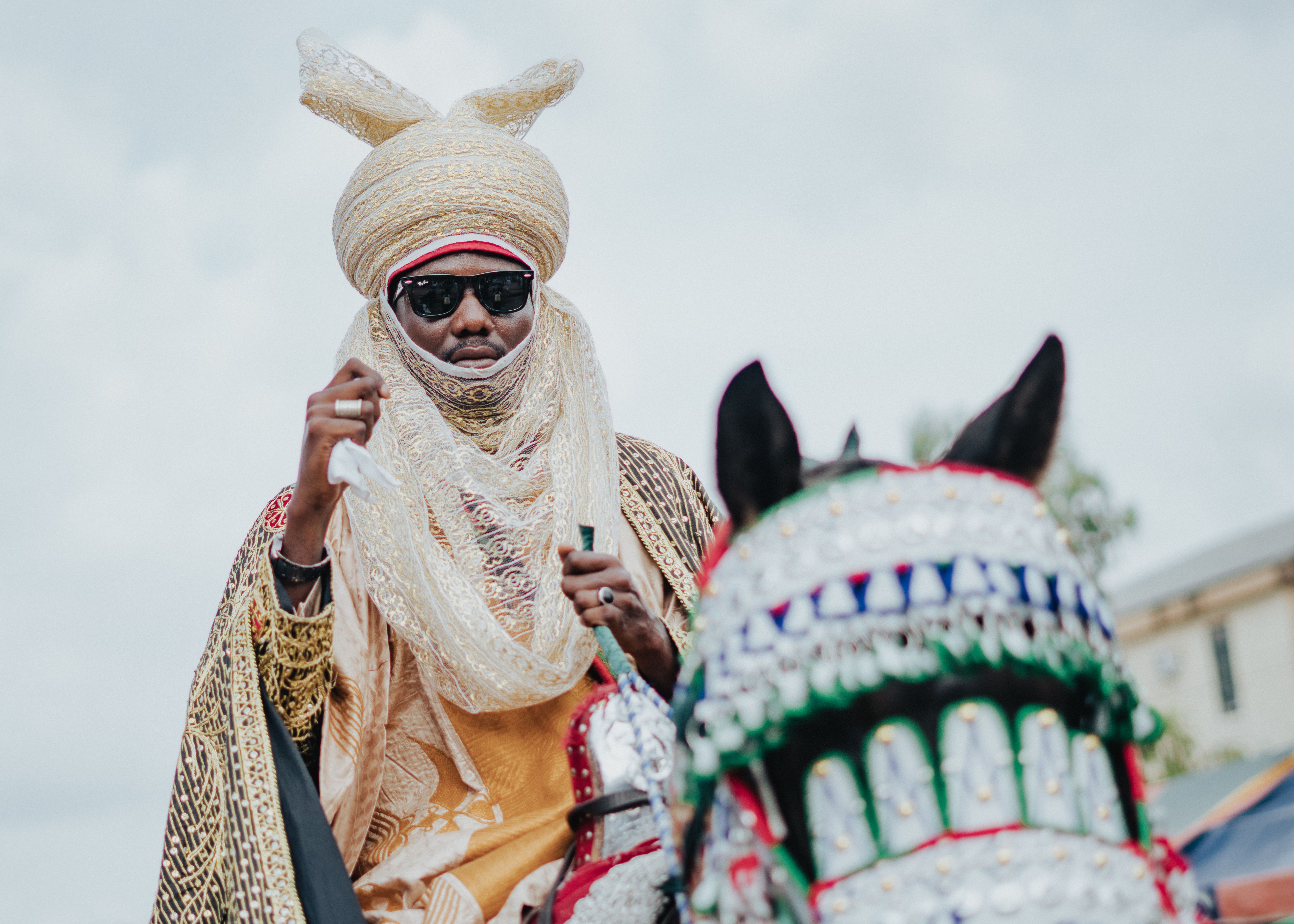 A man in traditional attire rides a elaborately decorated horse on a bright day.