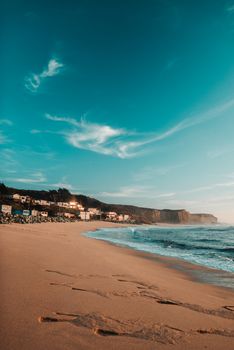 Calm sandy beach with blue waving sea and buildings on coastline under clear blue sky in morning time