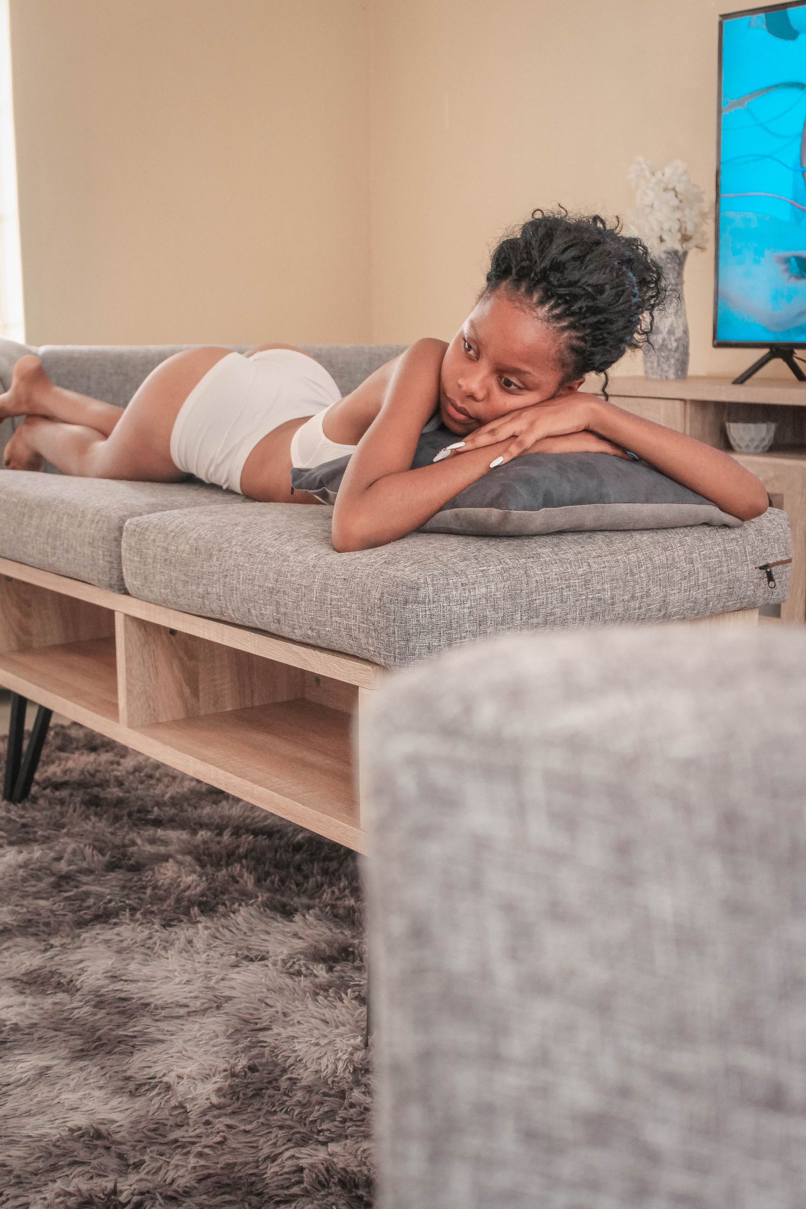 A Black woman rests on the sofa at home. Persistent fatigue is real and treatable, not something to push through.