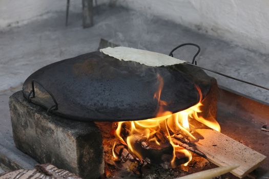 Flatbread cooking on an open fire using a metal skillet, showcasing rustic culinary techniques.