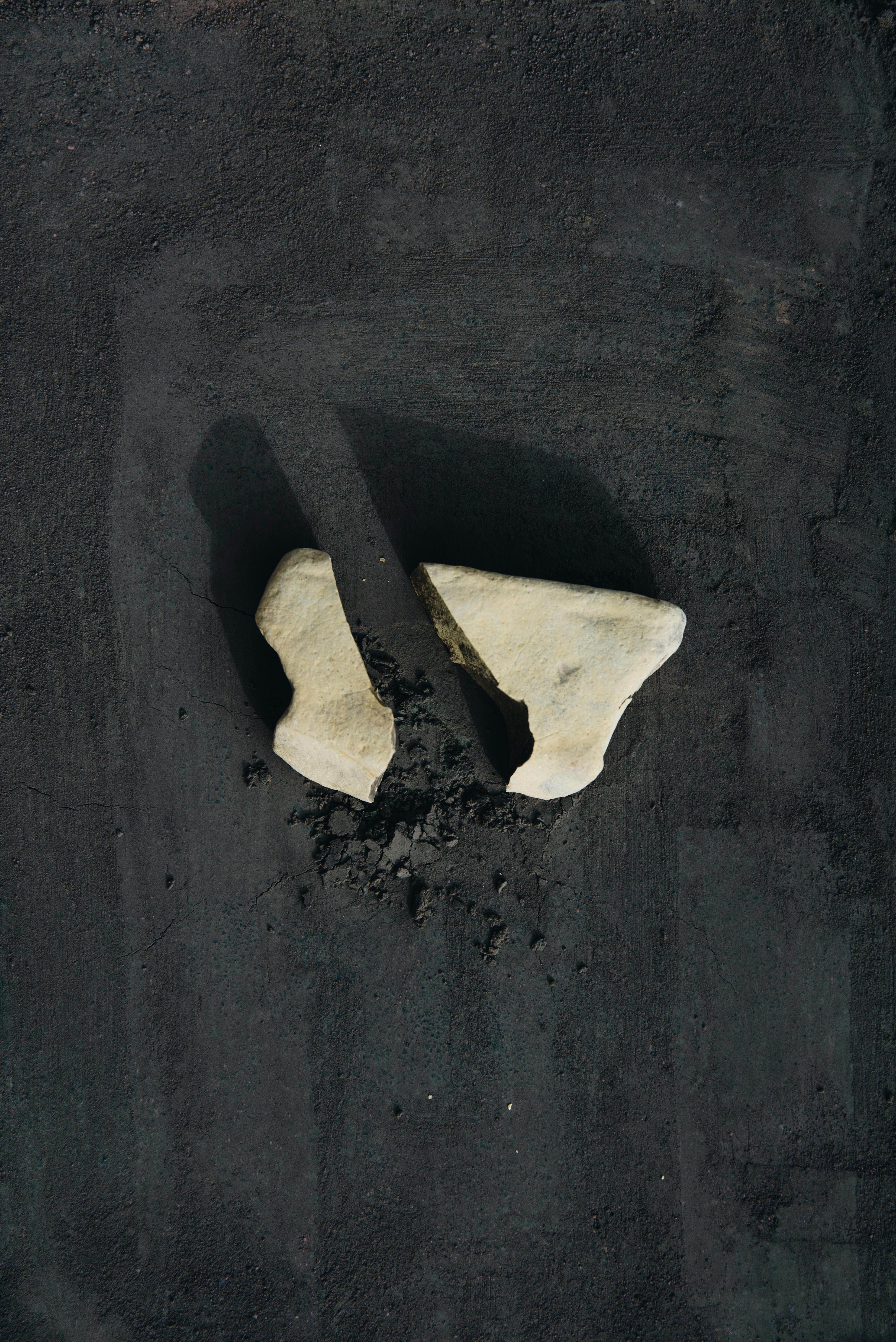 Broken stone pieces on a dark surface creating a conceptual minimalist still life shot.