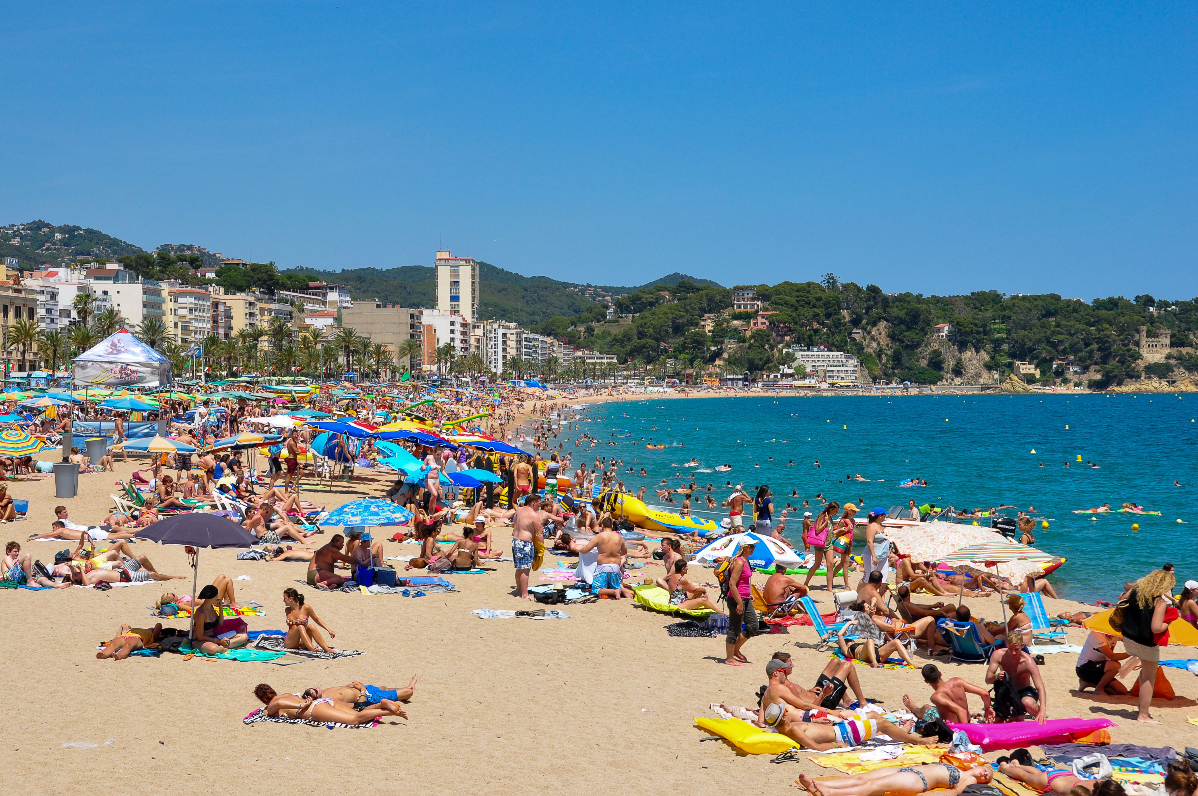 Experience the lively atmosphere of Lloret de Mar's sandy beach with vibrant parasols.