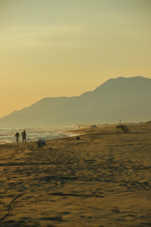 Free Sunset view of a serene beach in Antalya, Türkiye with silhouettes of people and mountains. Stock Photo