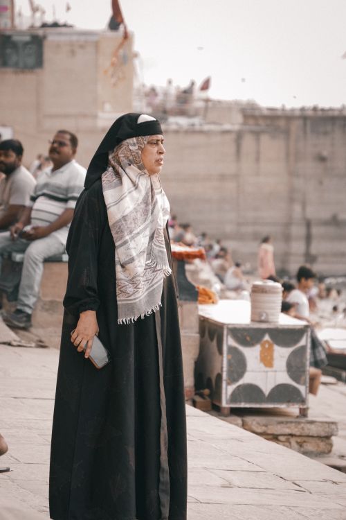 Free An elderly woman stands by the Ganges River in Varanasi, India, wearing traditional attire. Captured during the day. Stock Photo