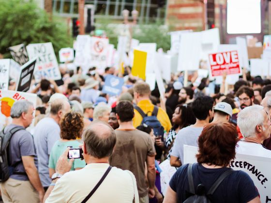 A crowd seen from behind carrying banners and placards in a city square