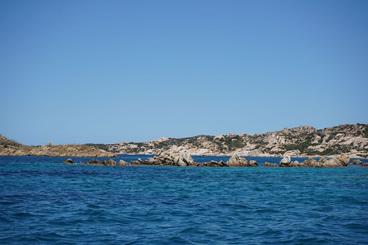 Linie joasa de insula granitica vazuta peste mare, sub cer curat