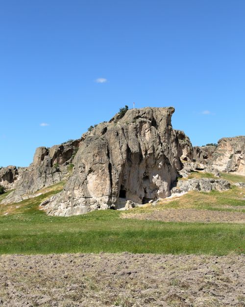 Free A stunning rocky outcrop towers over a grassy landscape beneath a bright blue sky. Stock Photo